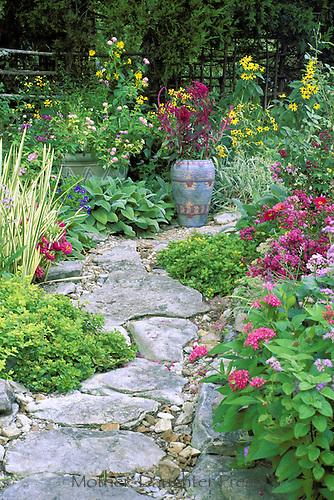 Rock pathway curves  through blooming garden of mult colored blooms and herbs with painted Mexican ceramic pot